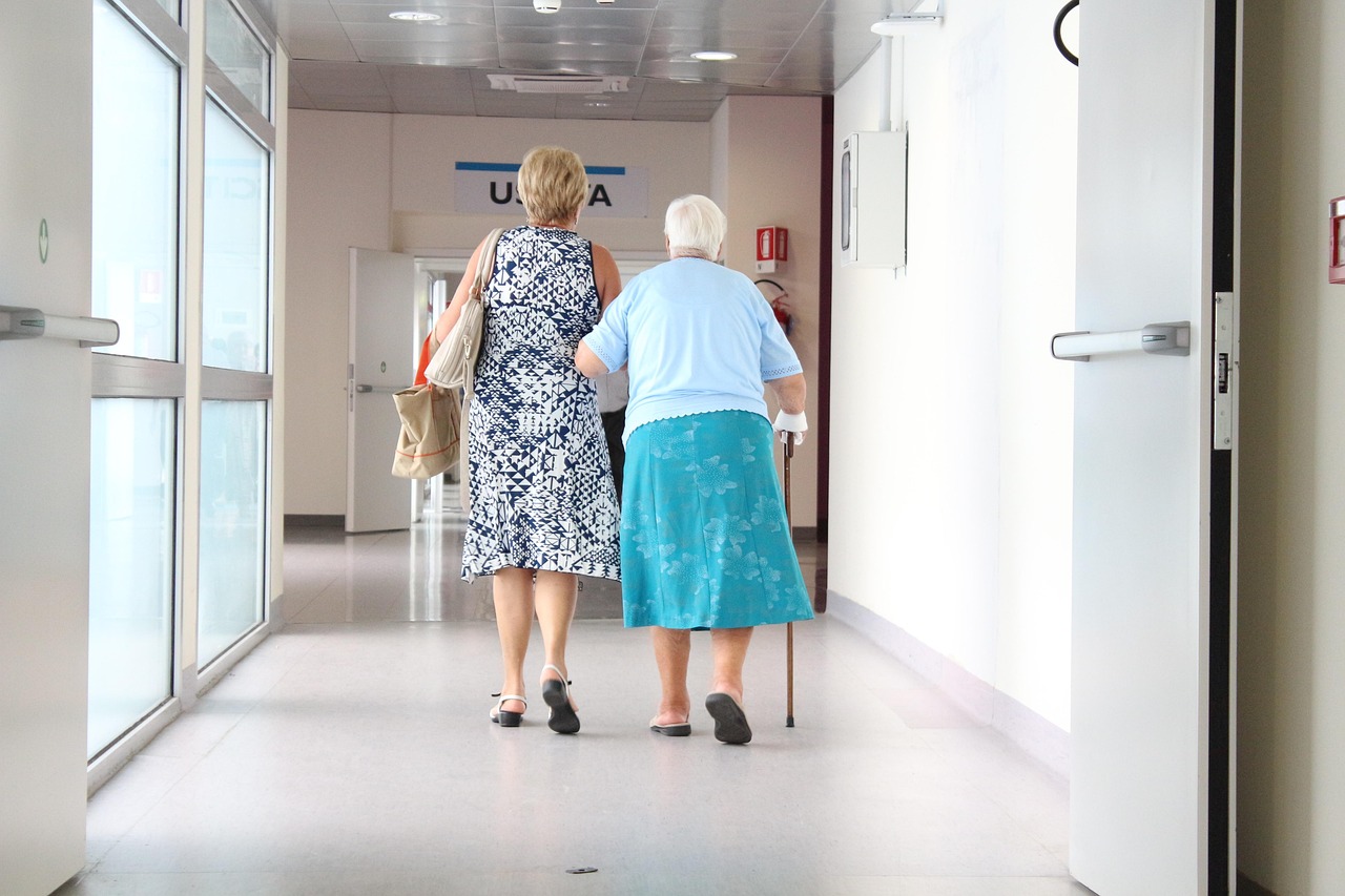 A woman walks with an older family member through a bright clinic hallway